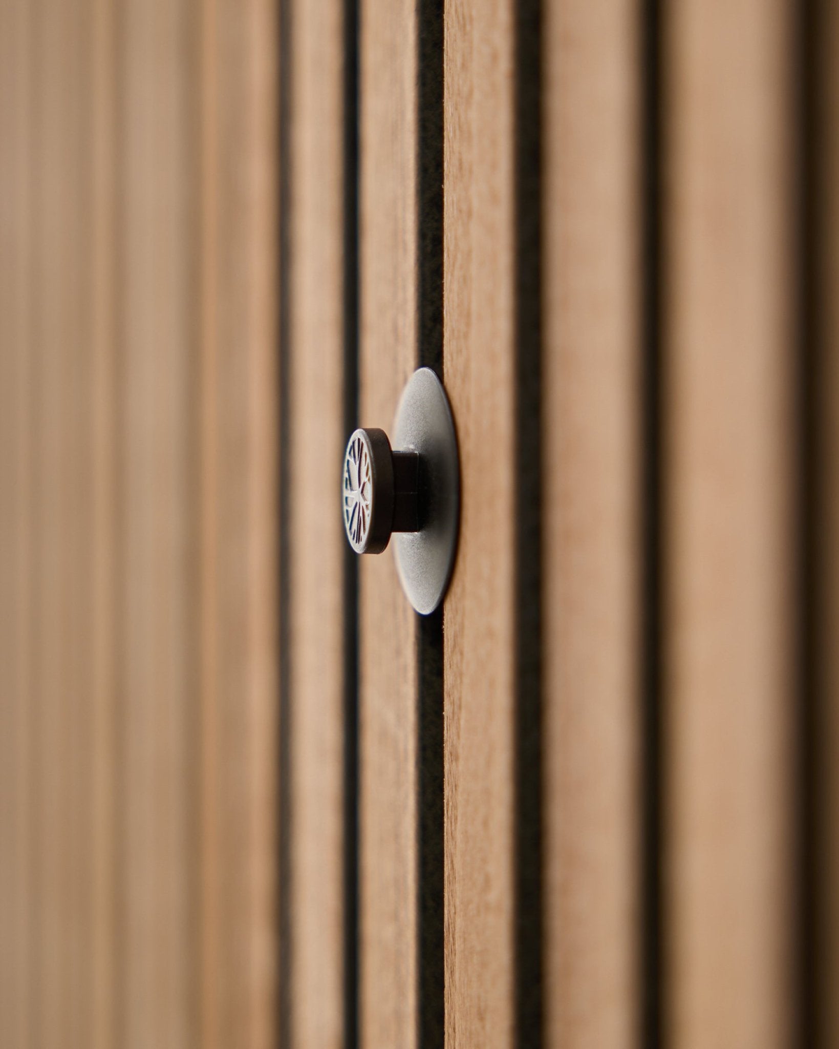 Primer plano de un Dupps | Light knob set (3 knobs plus tool) de WoodUpp instalado en un panel acústico de lamas, con las lamas de madera suavemente desenfocadas al fondo.